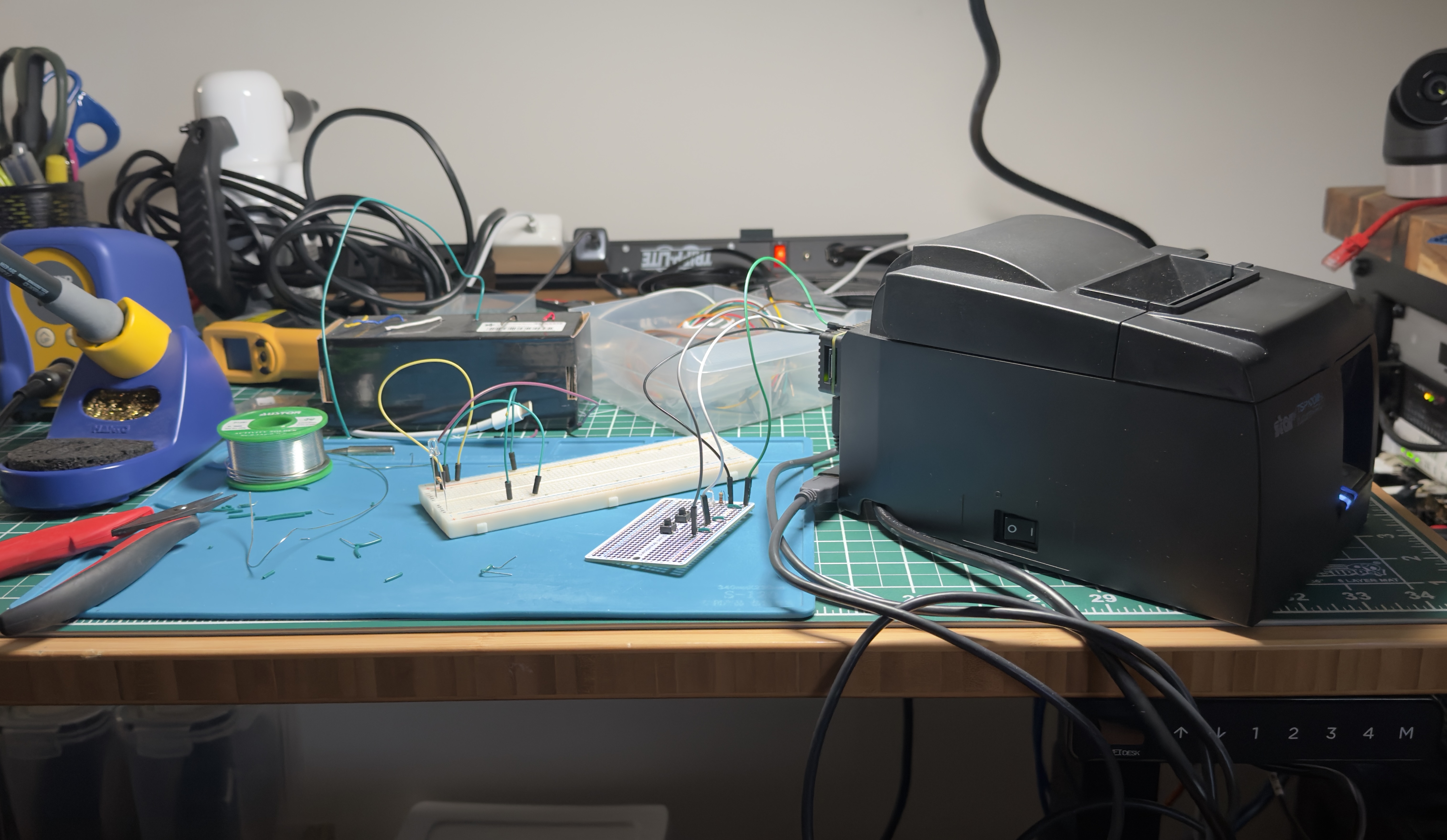 Thermal receipt printer beside the original breadboard prototype on the workbench